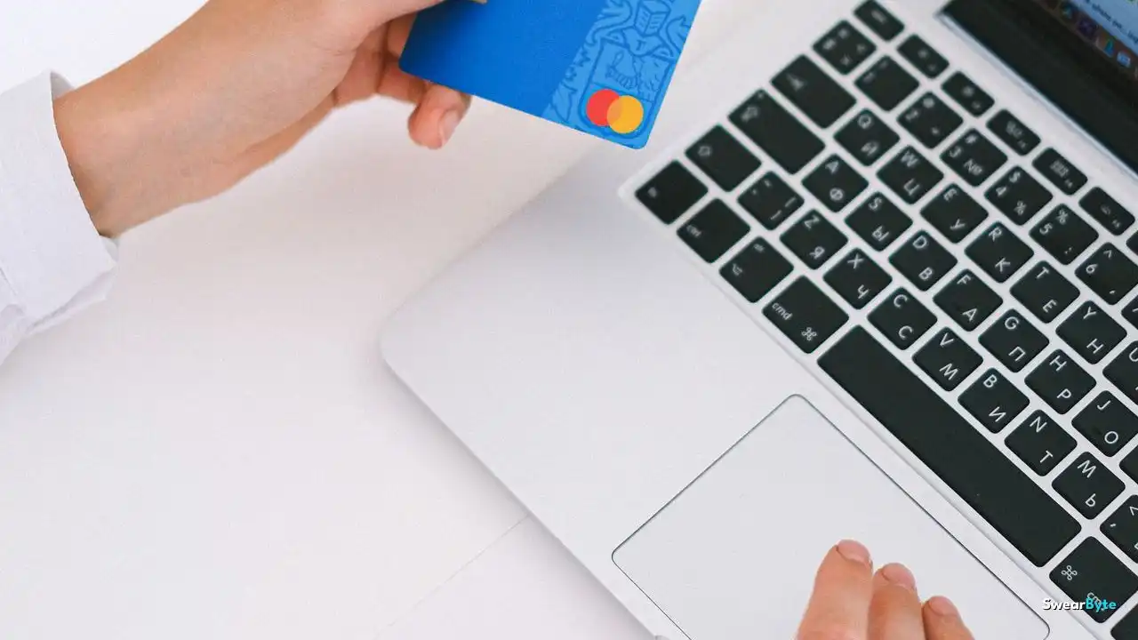 Hand holding a credit card near a laptop for online subscription billing